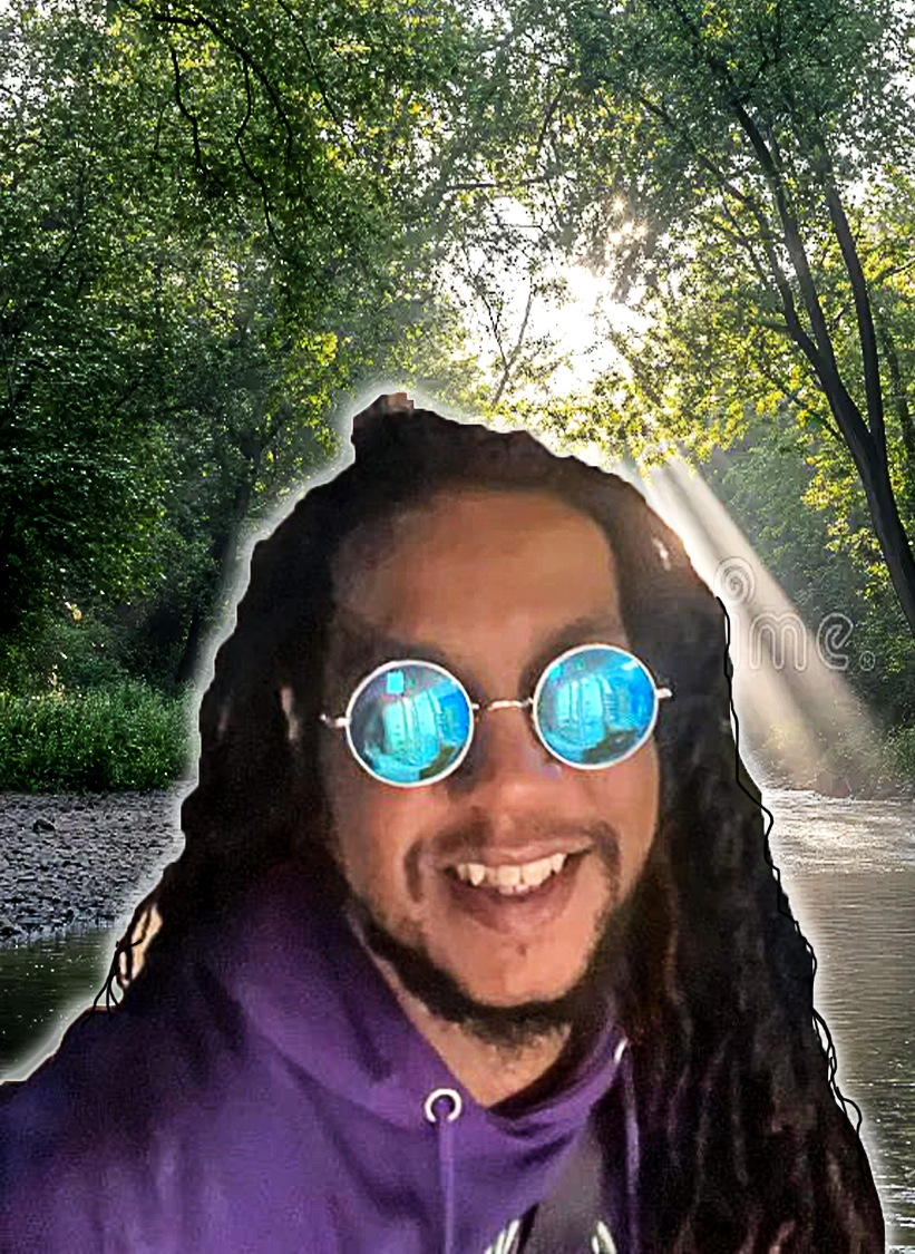 Kenny smiling by a sunlit river, wearing his signature round blue sunglasses